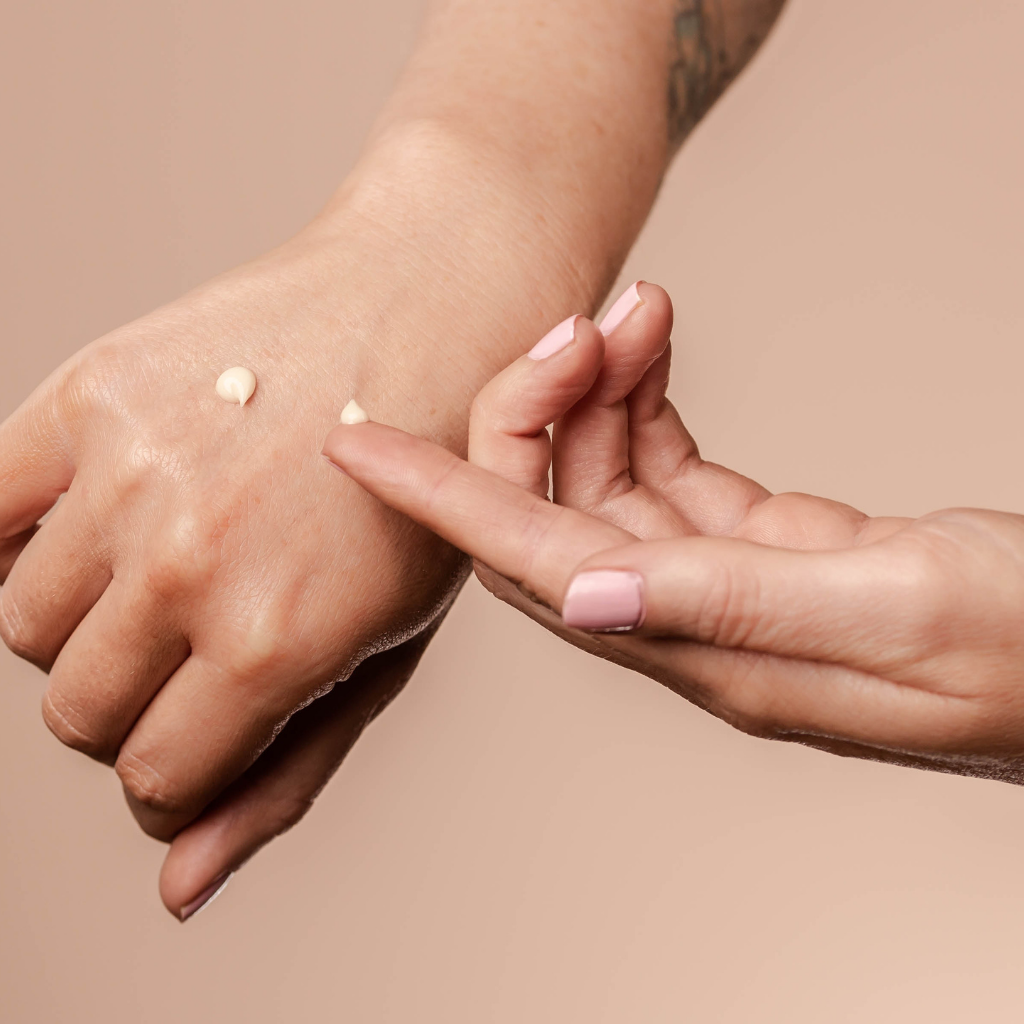 Woman dabbing organic under eye cream with white and green tea on back of hand