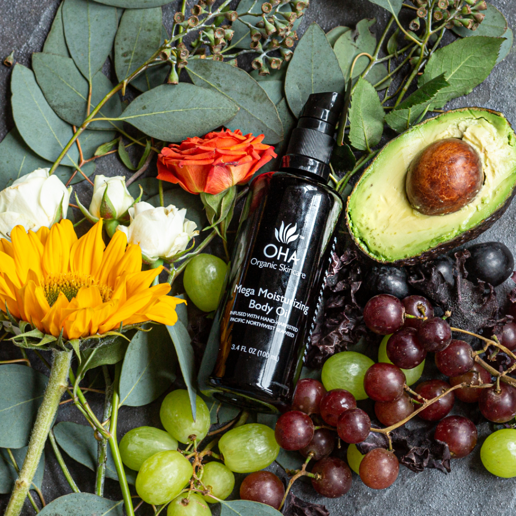 Organic hydrating body oil in a glass bottle on top of flowers and fruit assortment.