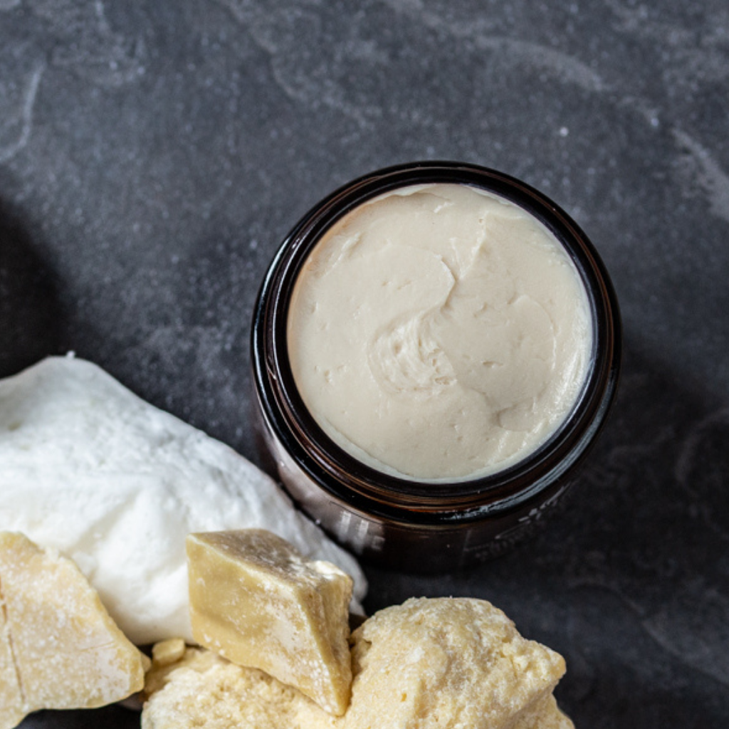 Luxurious organic cream with hand ground sugar and shea butter in a jar surrounded by shea butter 