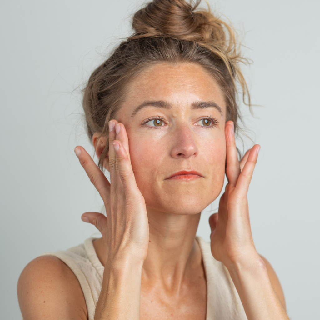 Woman applying skincare products to face.