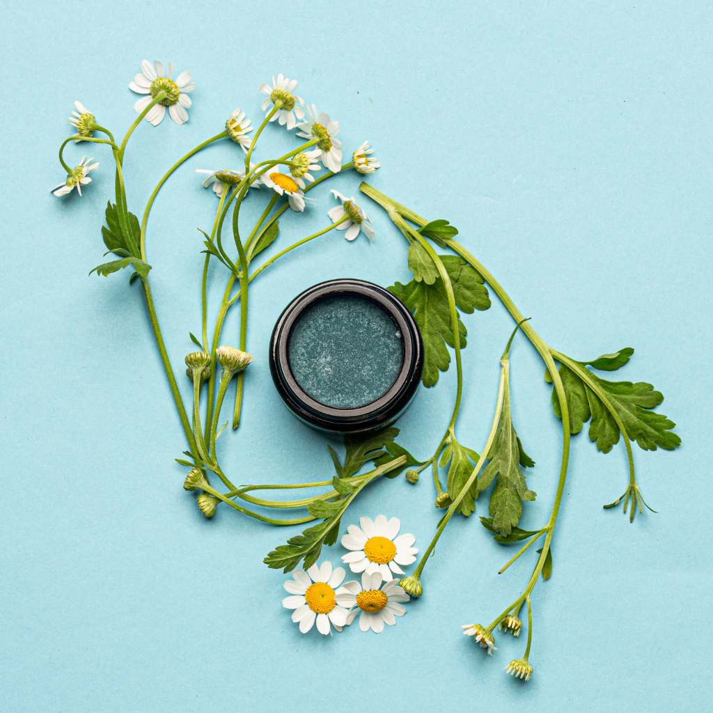 Blue soothing facial balm in black container surrounded by white and yellow flowers