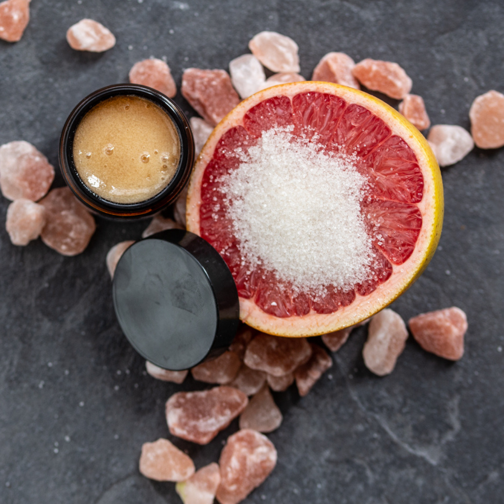 Organic facial sugar scrub in glass jar beside grapefruit with sprinkled sugar