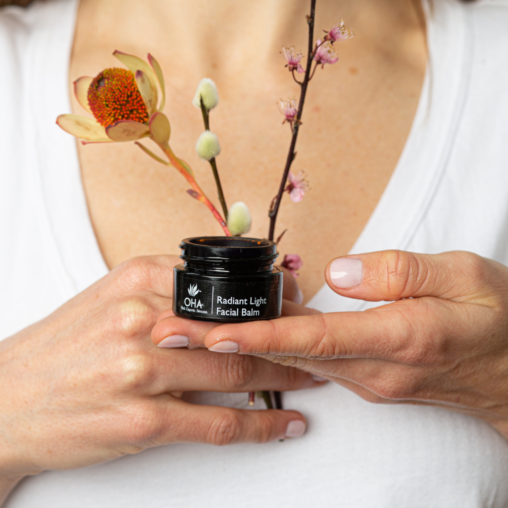 Woman holding jar of orange hydrating facial balm and florals