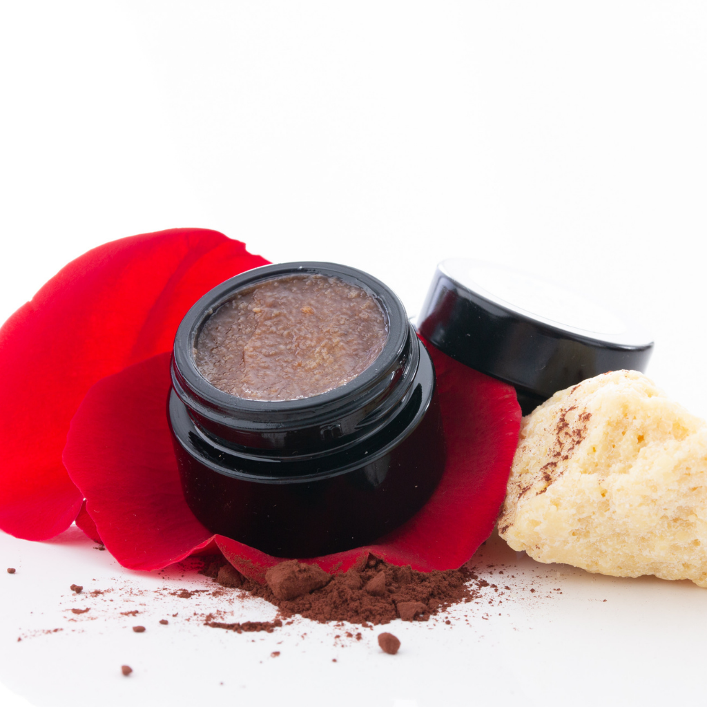 Chocolate &amp; rose lip balm in small glass jar on top of rose petal and cocoa dusting