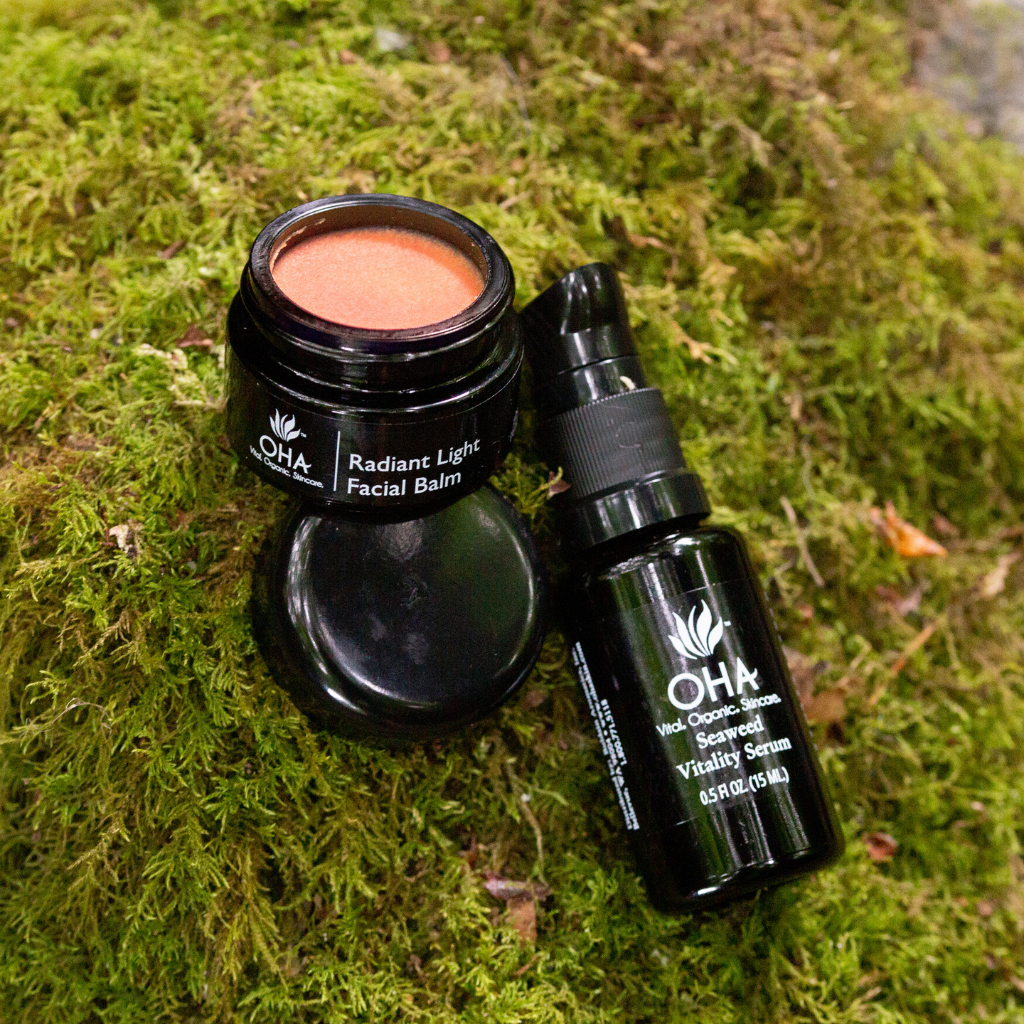 Pump bottle of Seaweed Vitality Serum and jar of Radiant Light Facial Balm sitting on mossy ground.